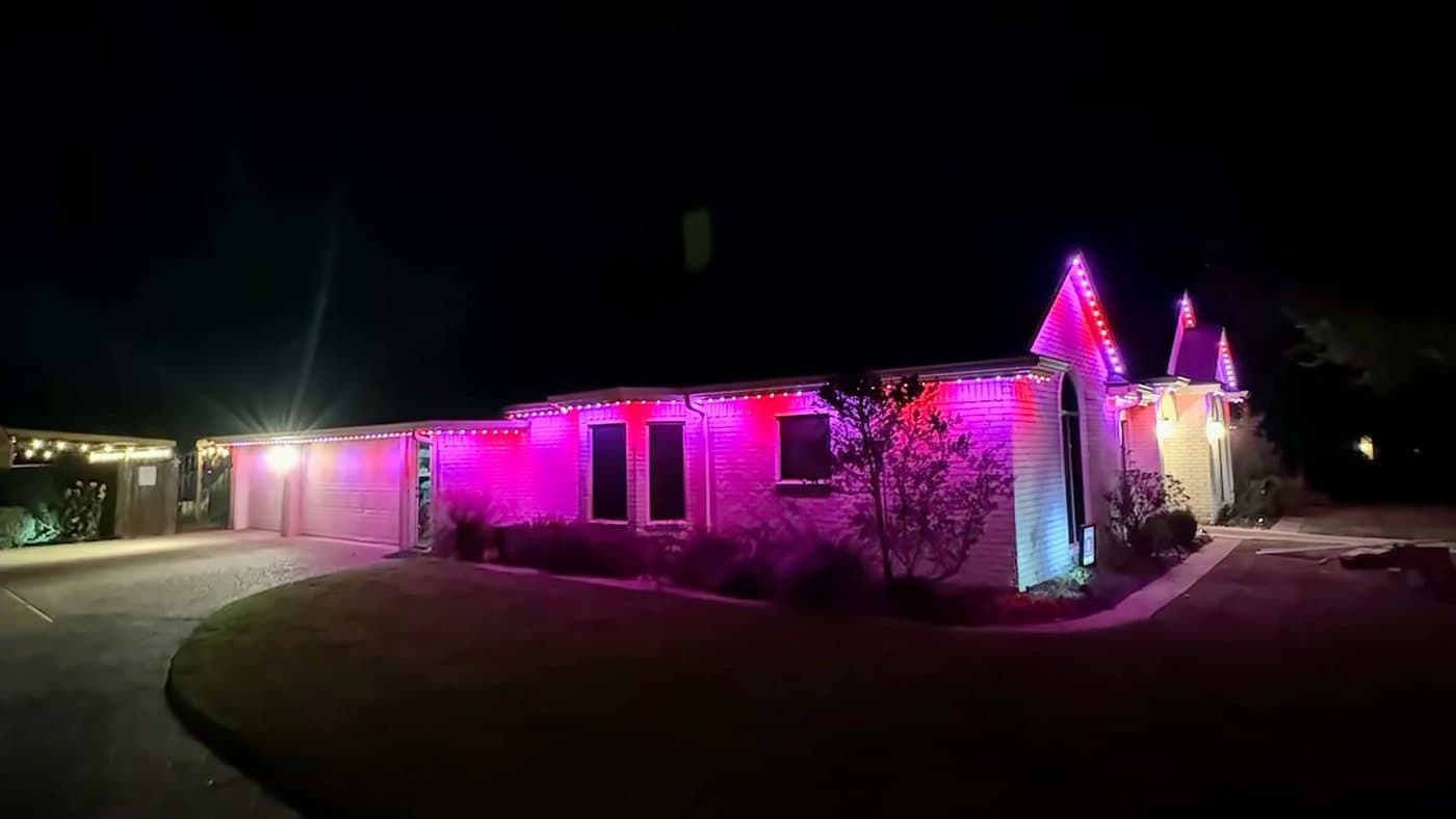A single-storey brick ranch home at night, its roofline and gables lit in magenta by permanent LED lighting