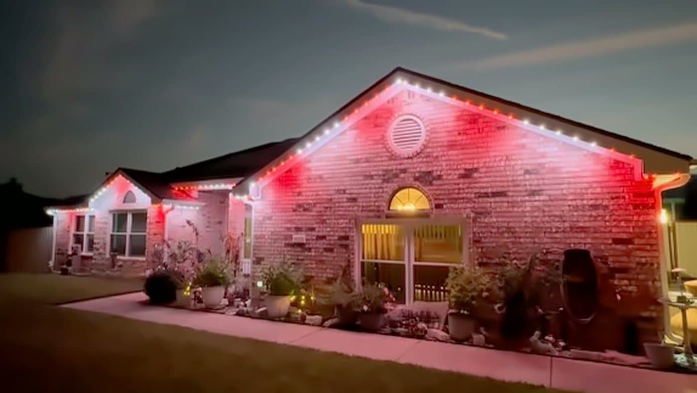 A brick home with a covered porch at dusk, roofline lit in red and warm white permanent LED lighting