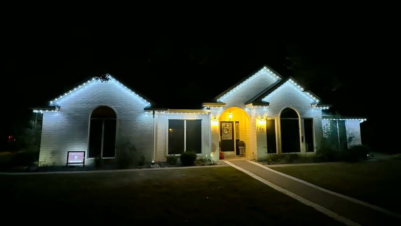 A white brick home at night with twin arched gables outlined in cool white permanent LED lighting