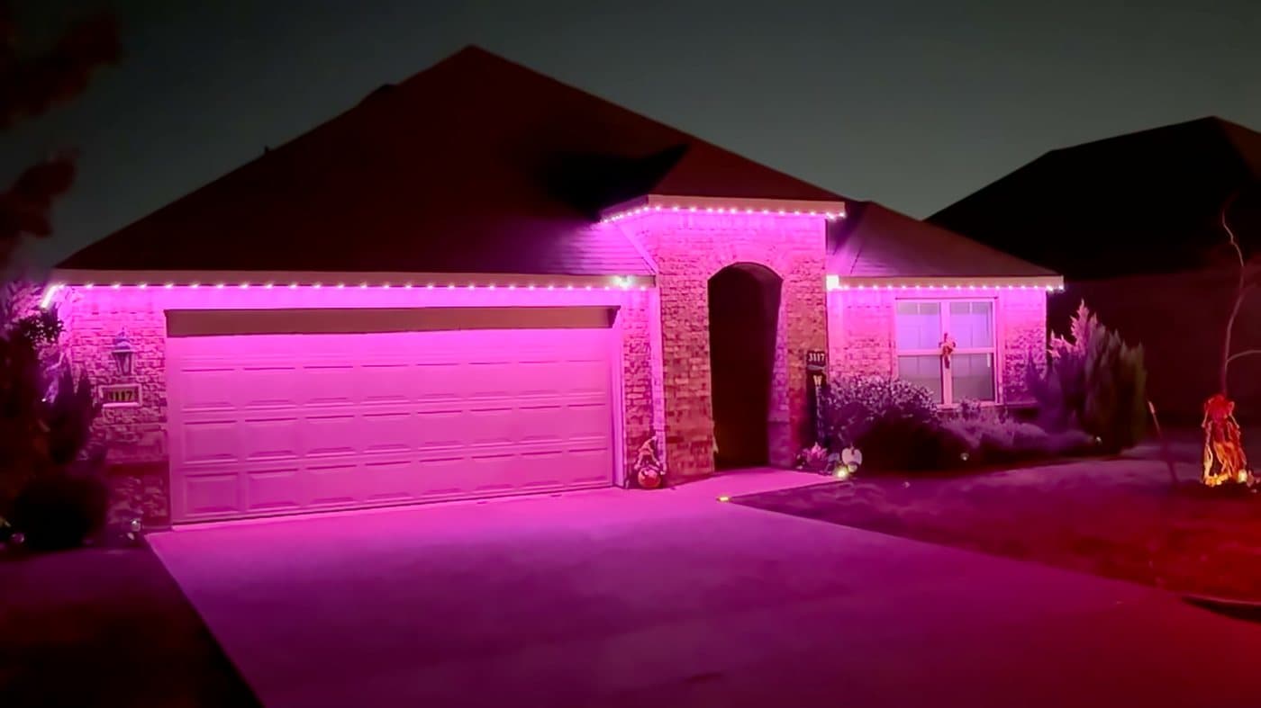 A brick home with a double garage at night, eaves and gable lit in magenta permanent LED lighting